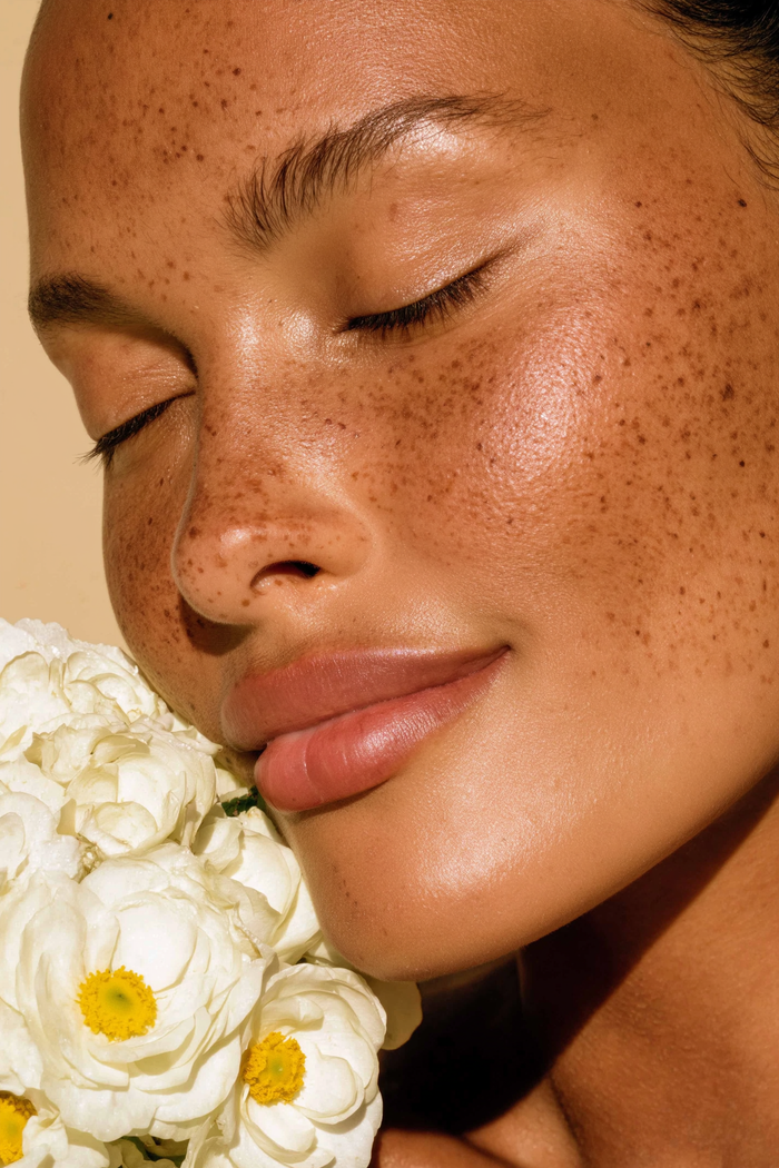 a tanned freckled woman softly smiling holding a bouquet of white flowers